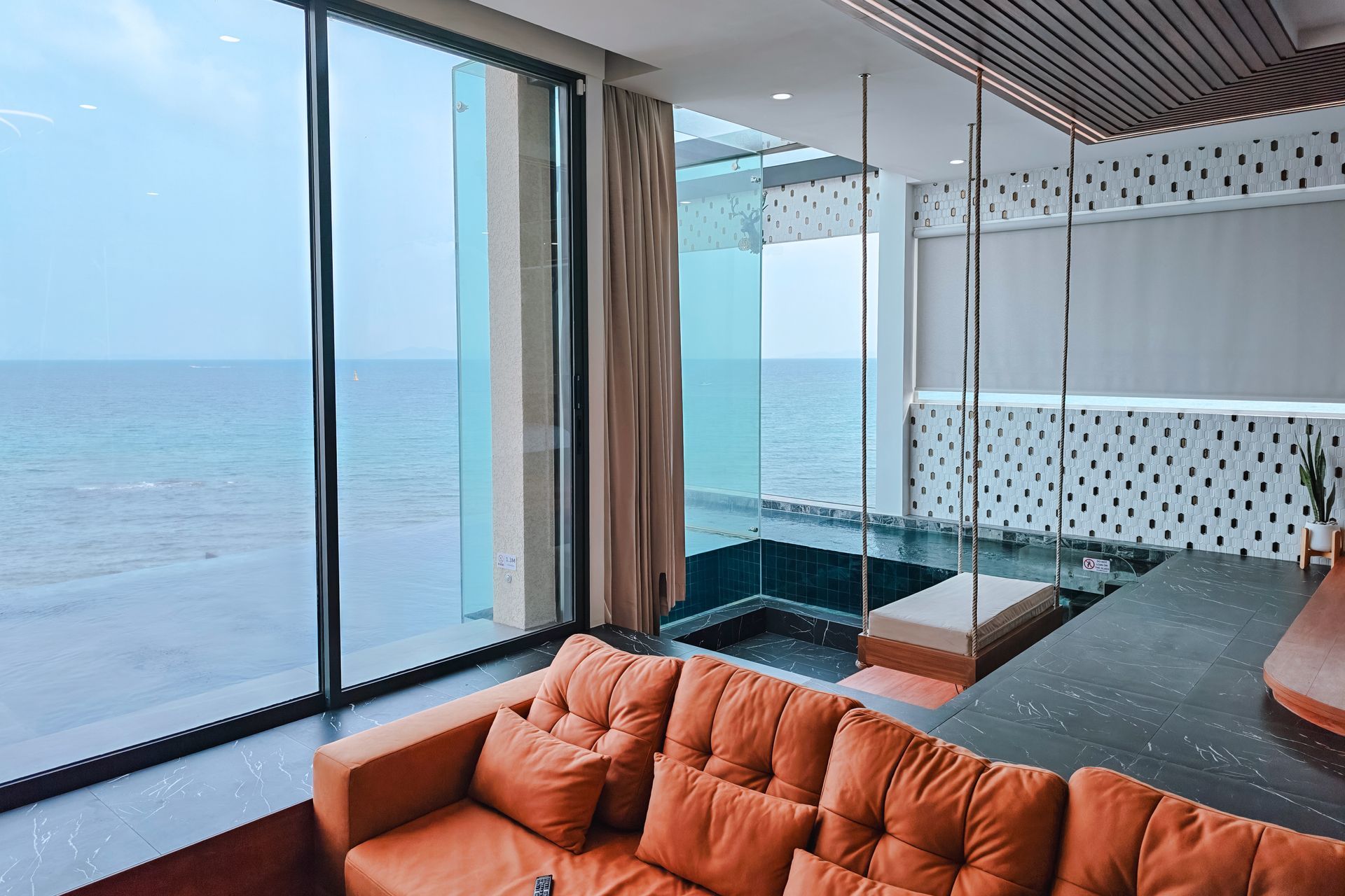 Living room with ocean view, orange sofa, swing, and large windows.