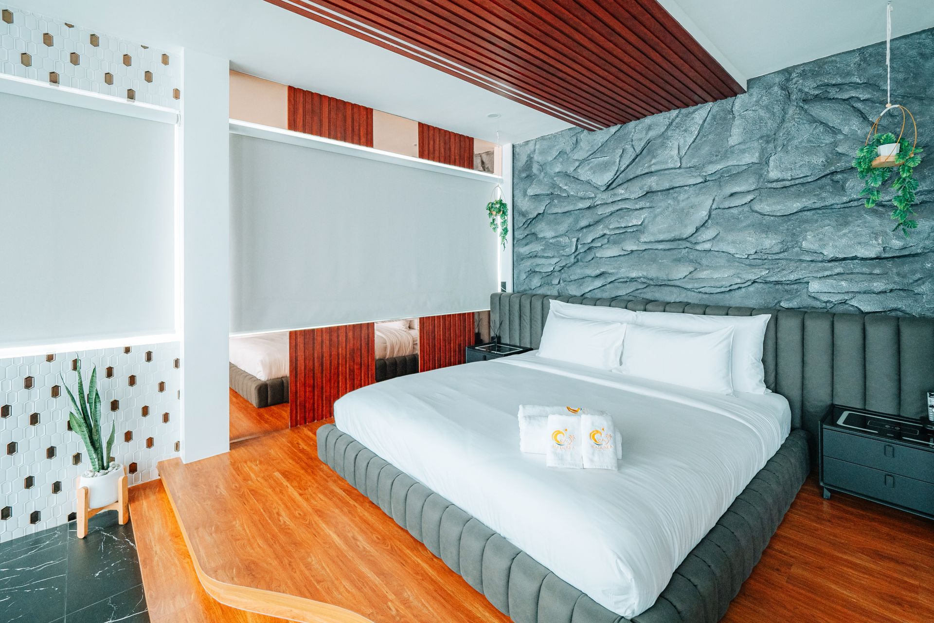 Modern hotel room with a stone accent wall, king-size bed, and wood flooring.