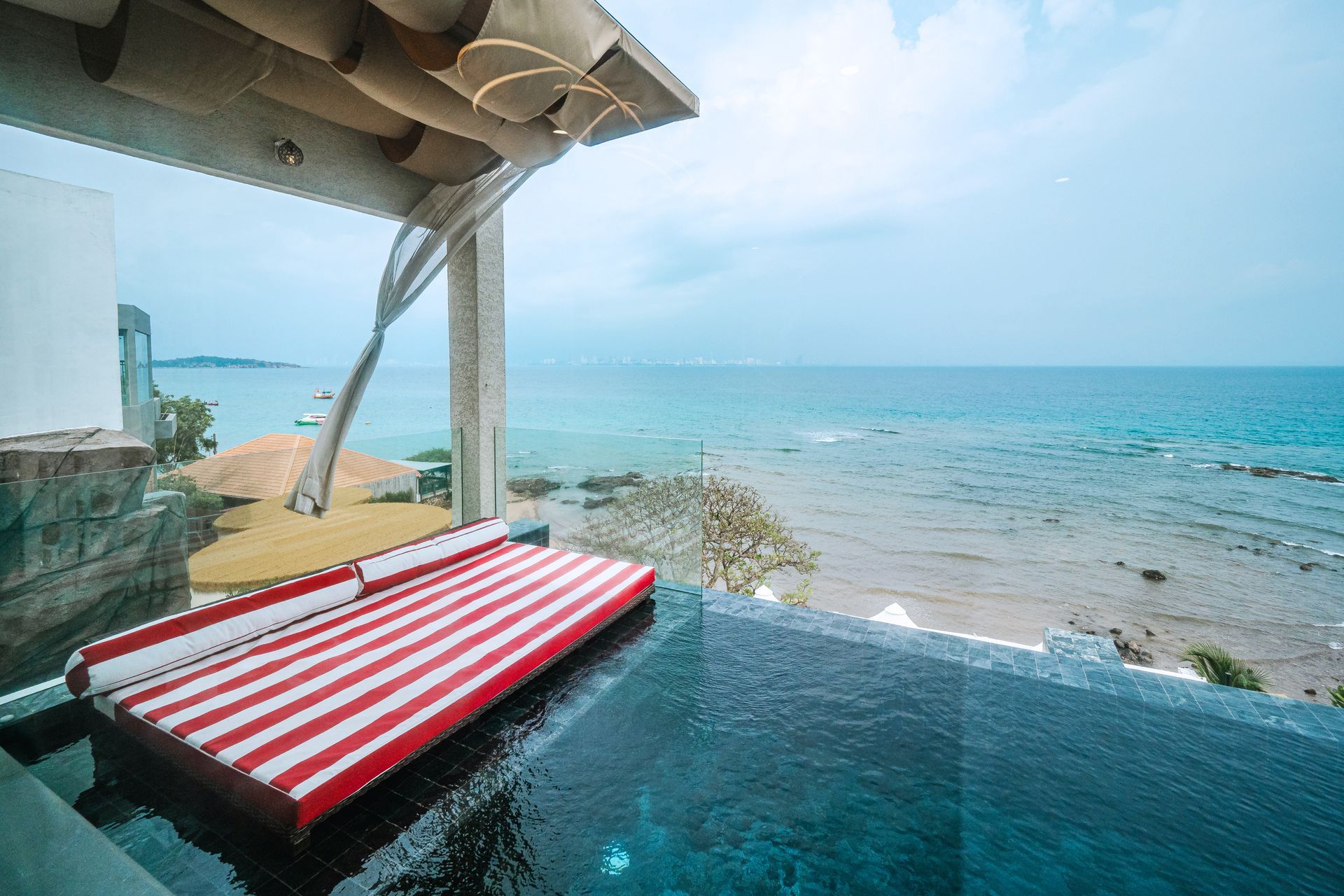Infinity pool with red and white striped cushions, overlooking a calm ocean.