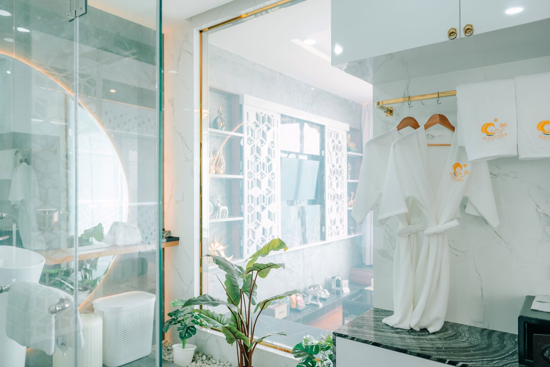 Luxurious bathroom with white robe and towels, marble accents, and greenery.