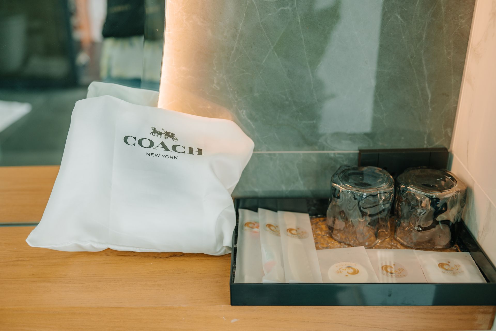Coach bag and toiletries on a wooden surface in a bathroom.