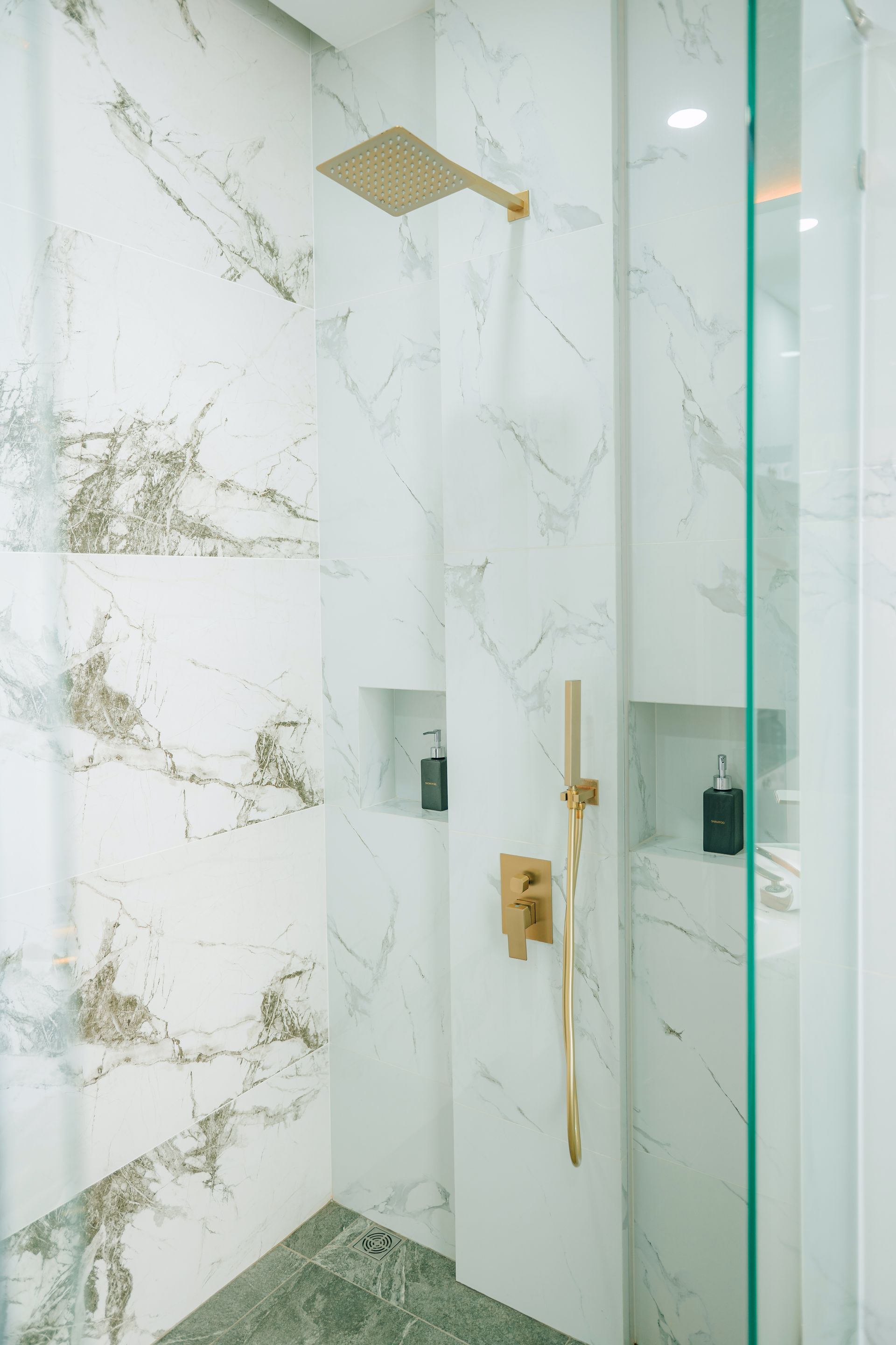 Luxurious white marble shower with gold fixtures and glass door.