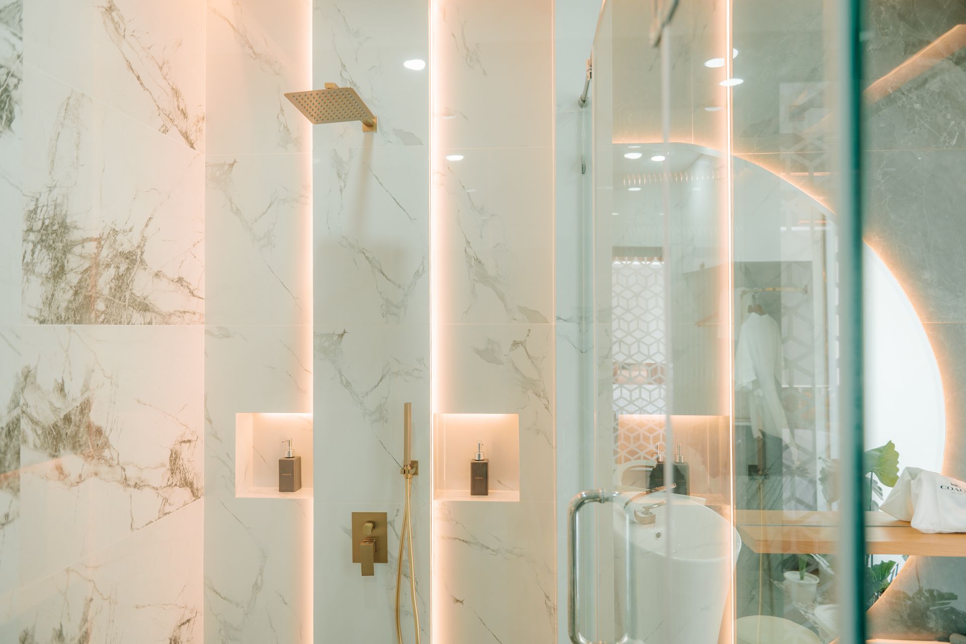 Luxurious marble shower with gold fixtures and built-in niches, glass door.