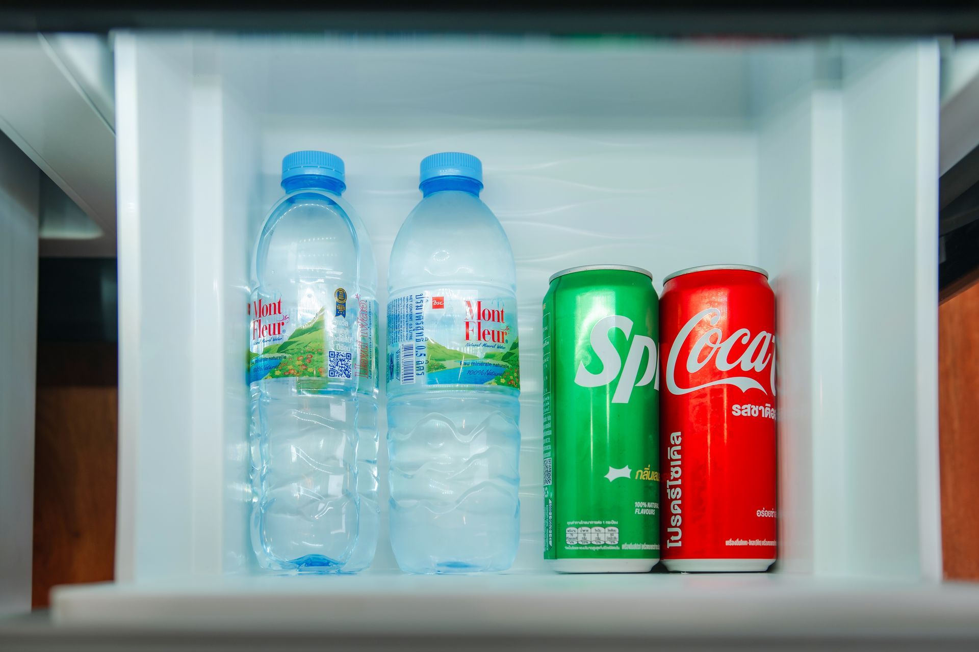 Bottled water and soda cans in a mini-fridge. Two water bottles, Sprite, and Coca-Cola.