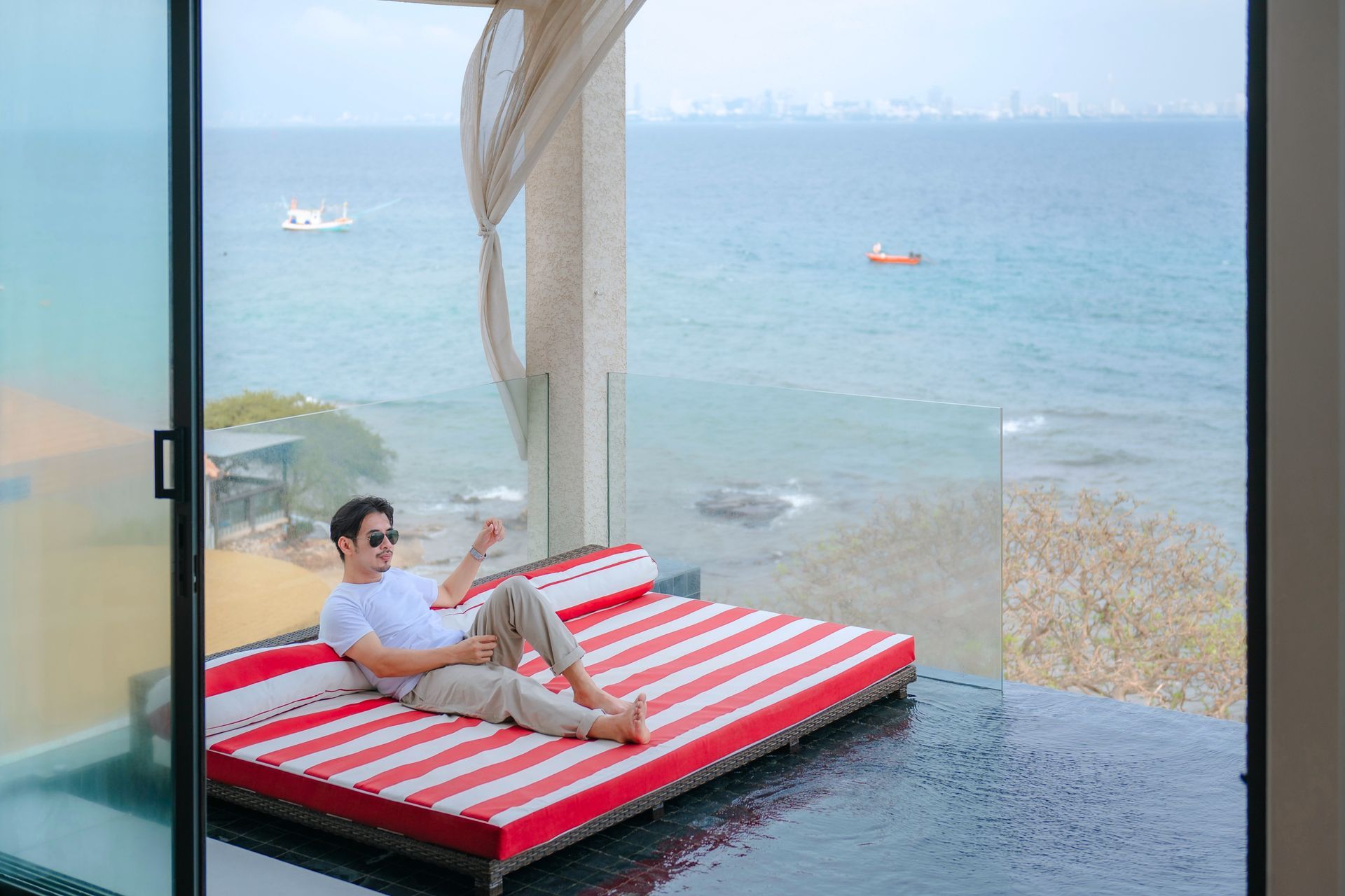 Man relaxes on a red-striped daybed by the ocean, pointing toward the water.