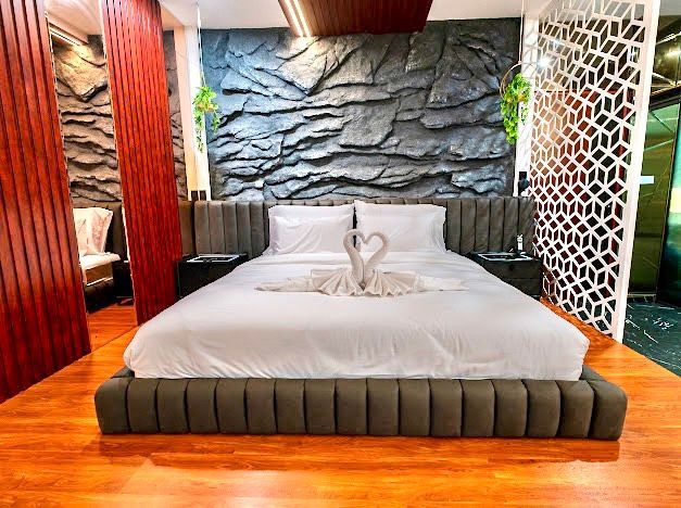 Bedroom with a bed, textured gray wall, and wood flooring. Features include swan towel art and decorative panel.