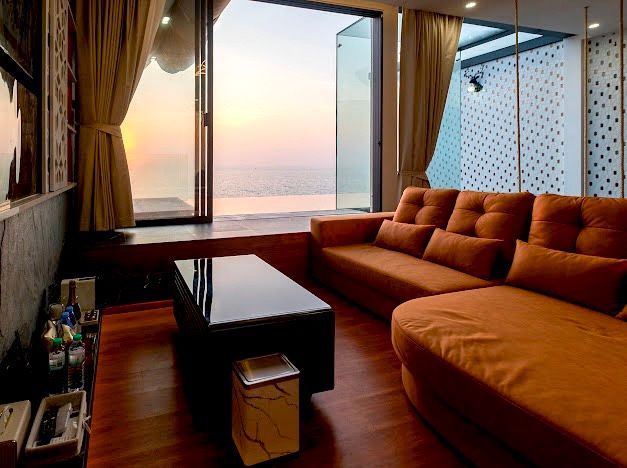 Living room with orange sofa and open doors overlooking ocean at sunset.