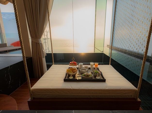Breakfast tray on a hanging bed, overlooking a seascape at sunset.