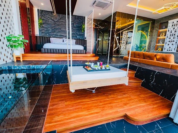 Luxurious bedroom with swing bed over pool; bed, seating, dark flooring, and decorative walls.