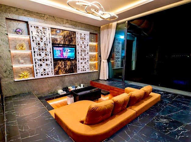 Modern living room with orange sunken sofa, decorative wall, dark floor, and large window.