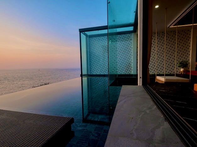 Infinity pool overlooking ocean at sunset; modern glass-walled room with swing.