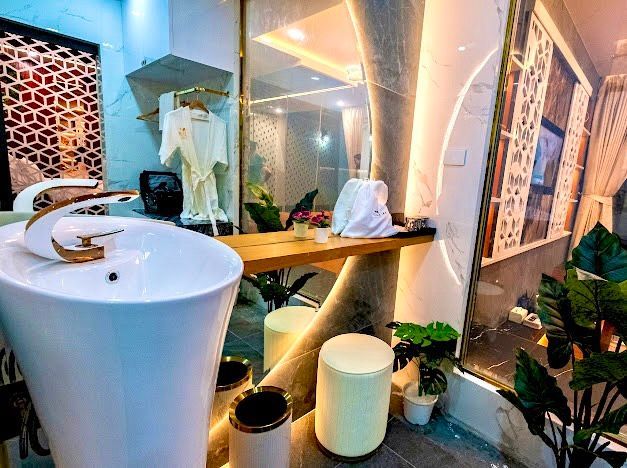 Luxurious bathroom with white sink, gold faucet, marble walls, and decorative plants.