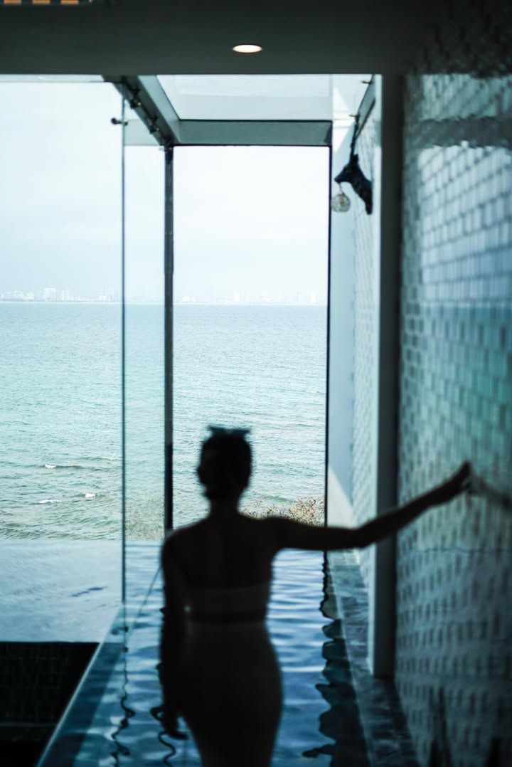 Silhouette of a person in a pool overlooking the ocean. They touch a textured wall, arm outstretched.