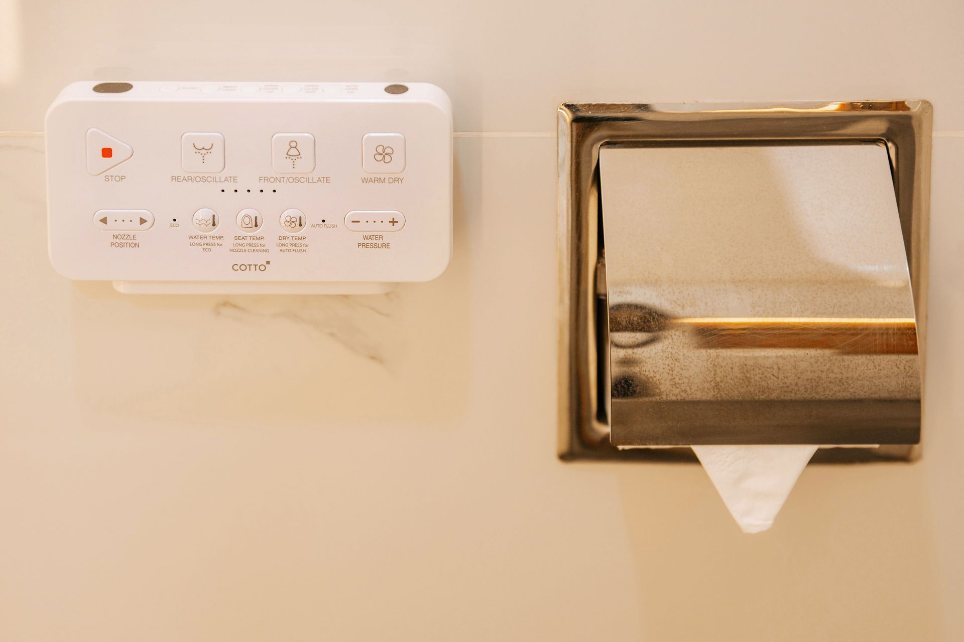 White control panel and stainless steel tissue dispenser mounted on a beige wall.