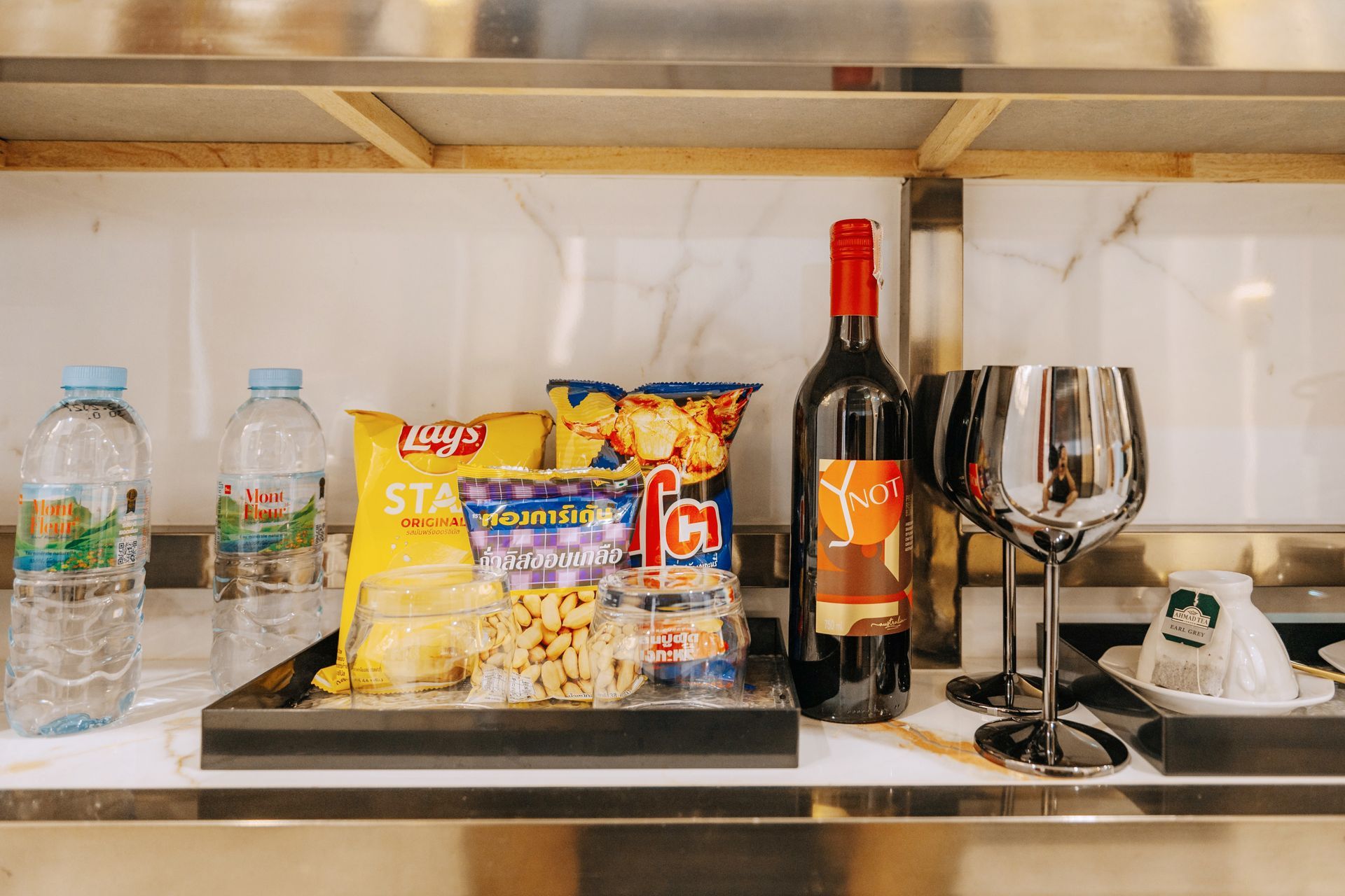 Bottled water, snacks, wine bottle, and glasses arranged on a tray on a shelf.