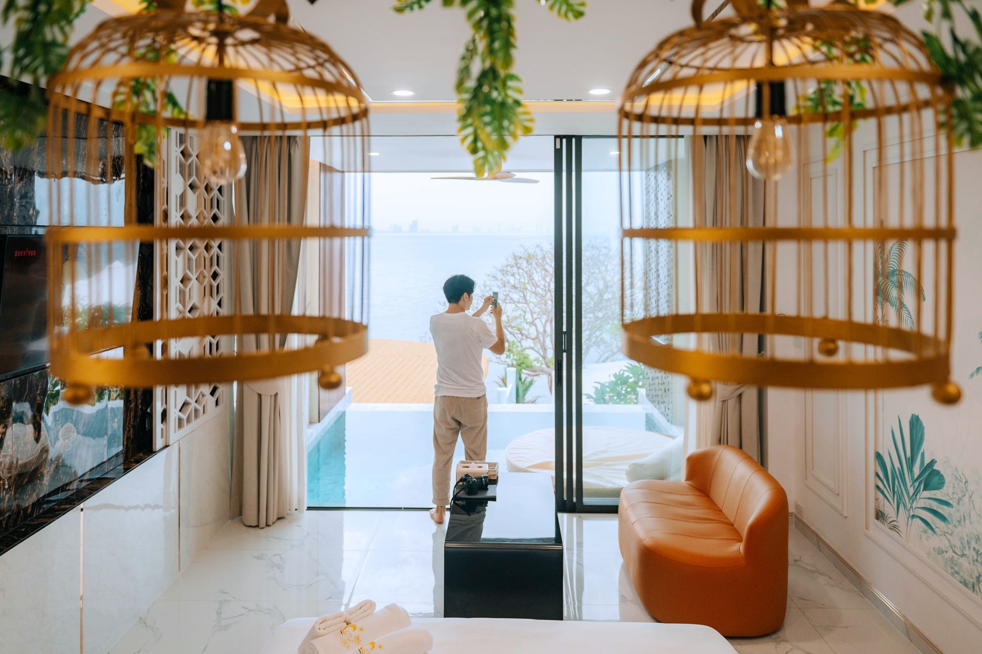 Man taking photo by pool from luxury interior with birdcage lights.