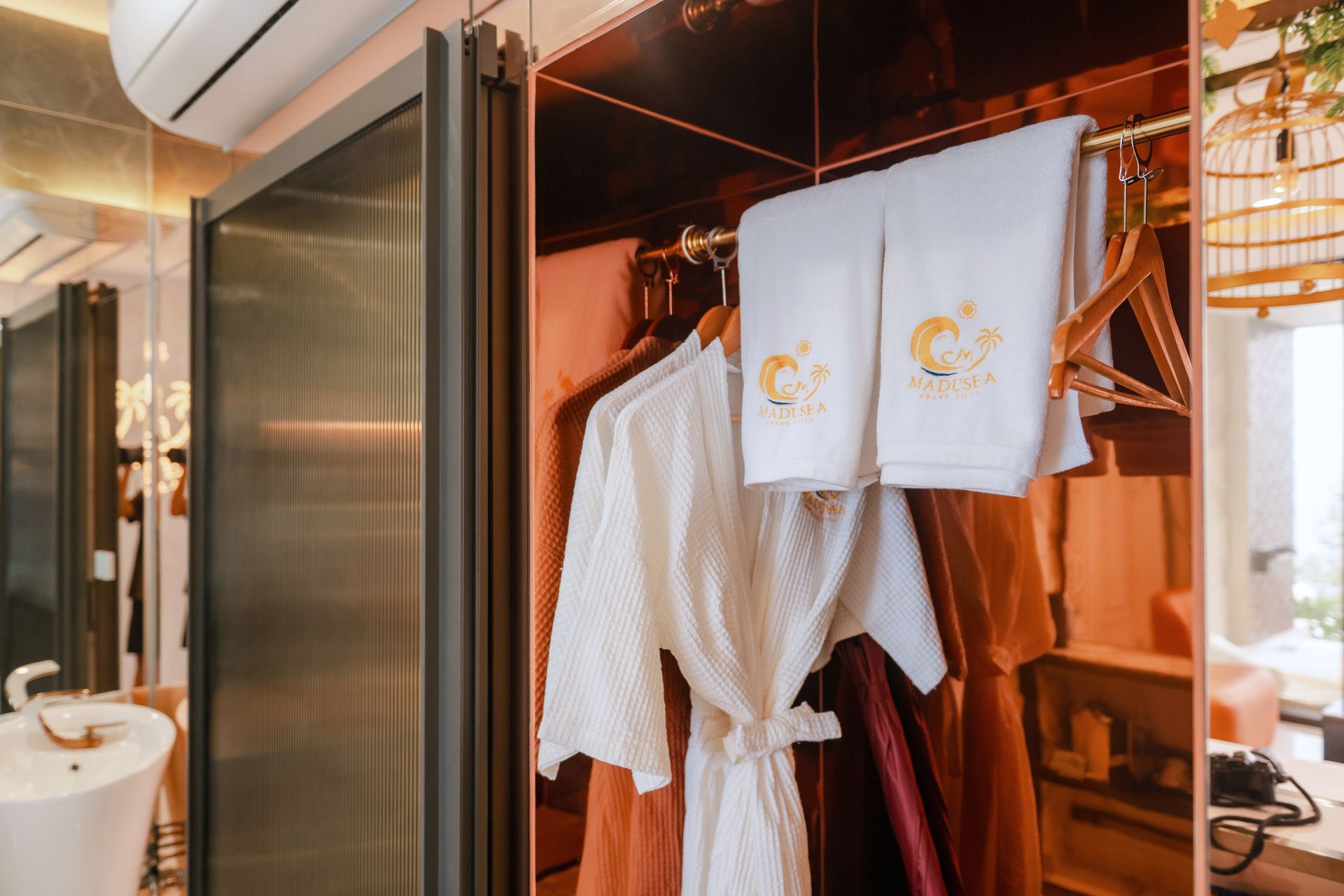 Closet with white bathrobe, towels, and clothing; gold rod; copper-toned doors and trim.