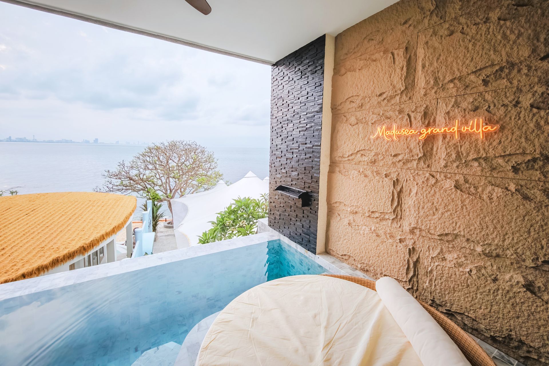 A balcony with a small pool overlooking the ocean. The textured wall has neon text.