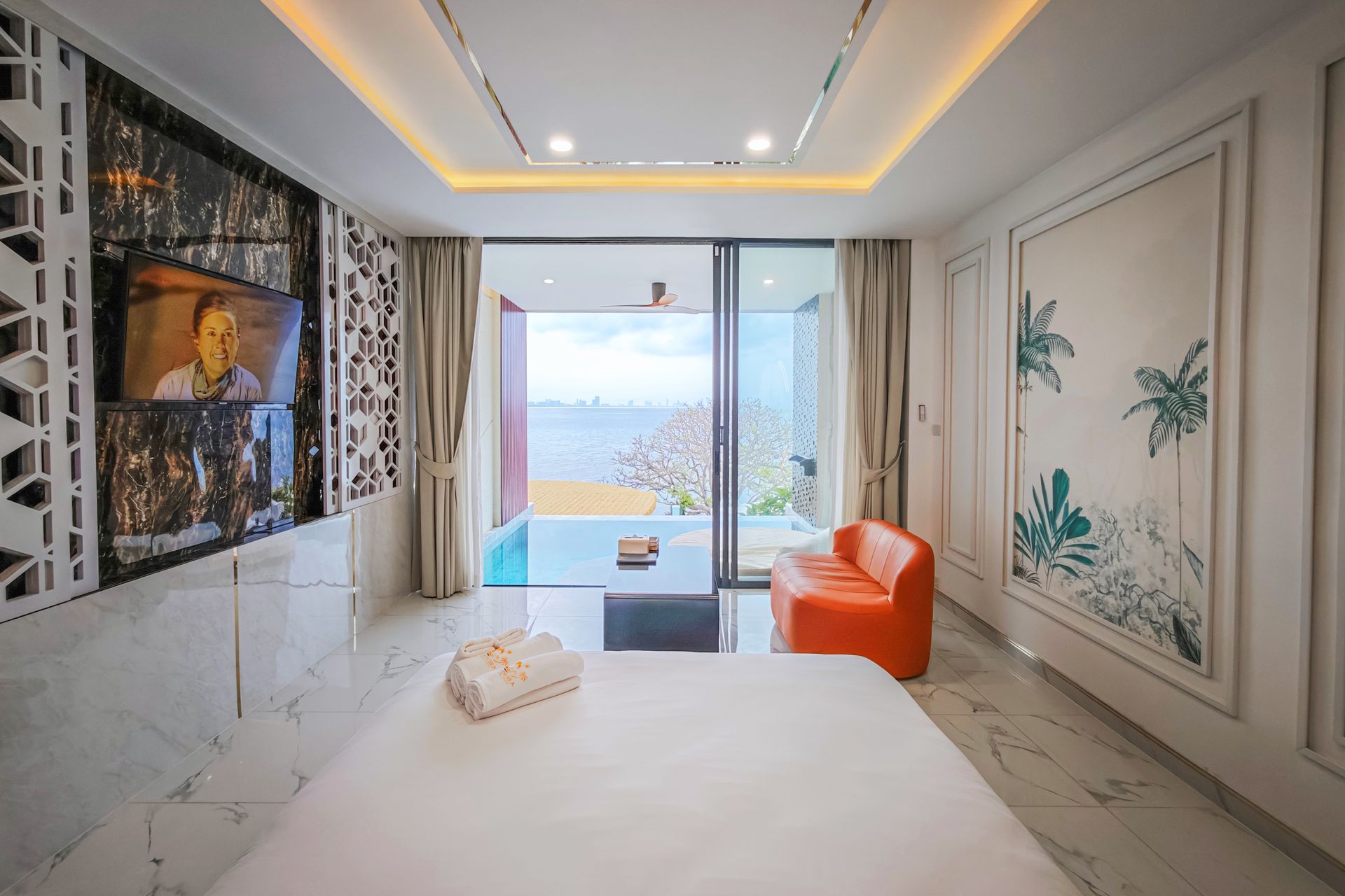 Bedroom with a bed, TV, orange chair, and view of a pool and the ocean.