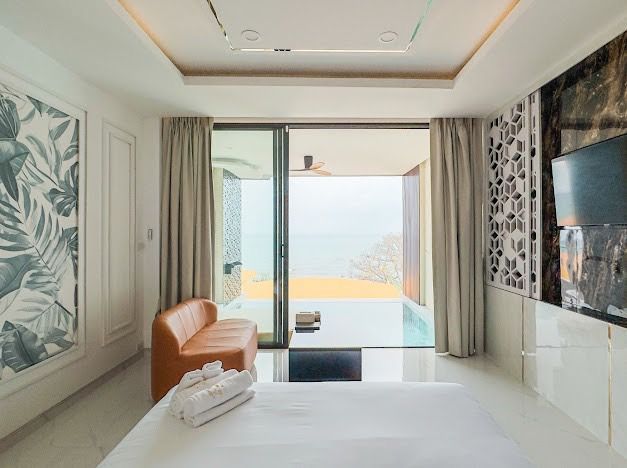 Bedroom with ocean view, pool access, orange couch, white bed, large window, and decorative wall art.