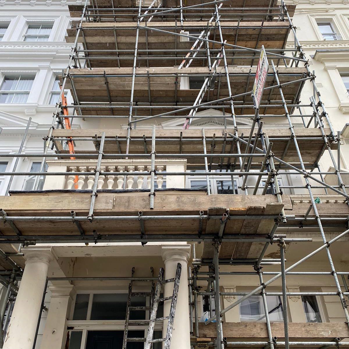 Scaffolding covering a building's facade during renovation. Beige building, white trim, and construction activity.
