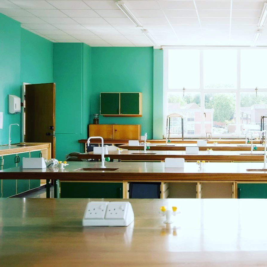 Empty teal-walled science lab with long wooden tables, sinks, and large windows.