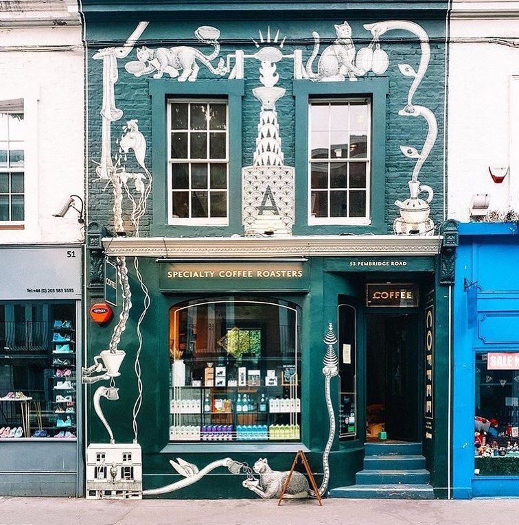 Green coffee shop facade with white artwork, steps, and a wooden sign.
