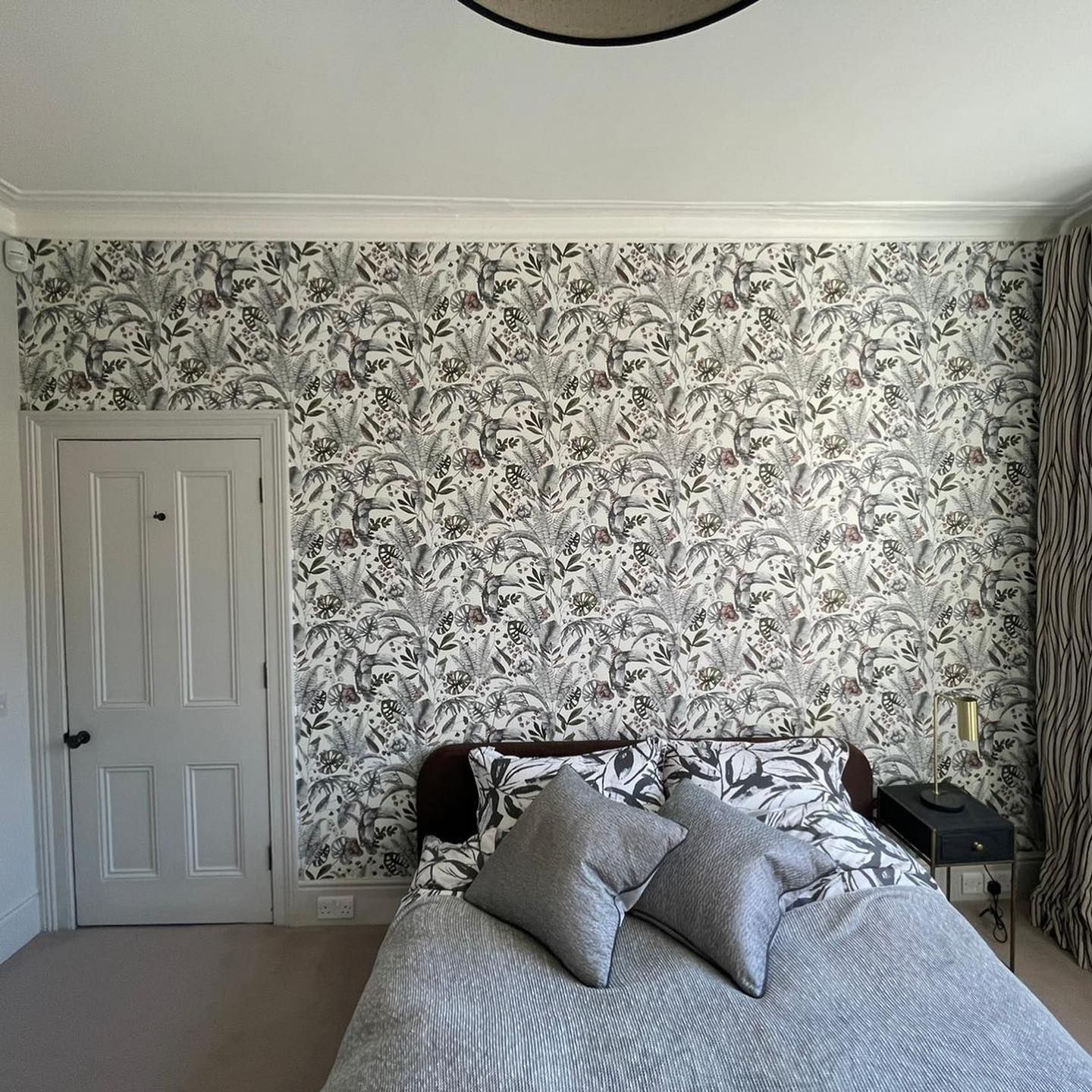 Bedroom with patterned wallpaper, bed with gray pillows and bedding, closed door, and patterned curtains.
