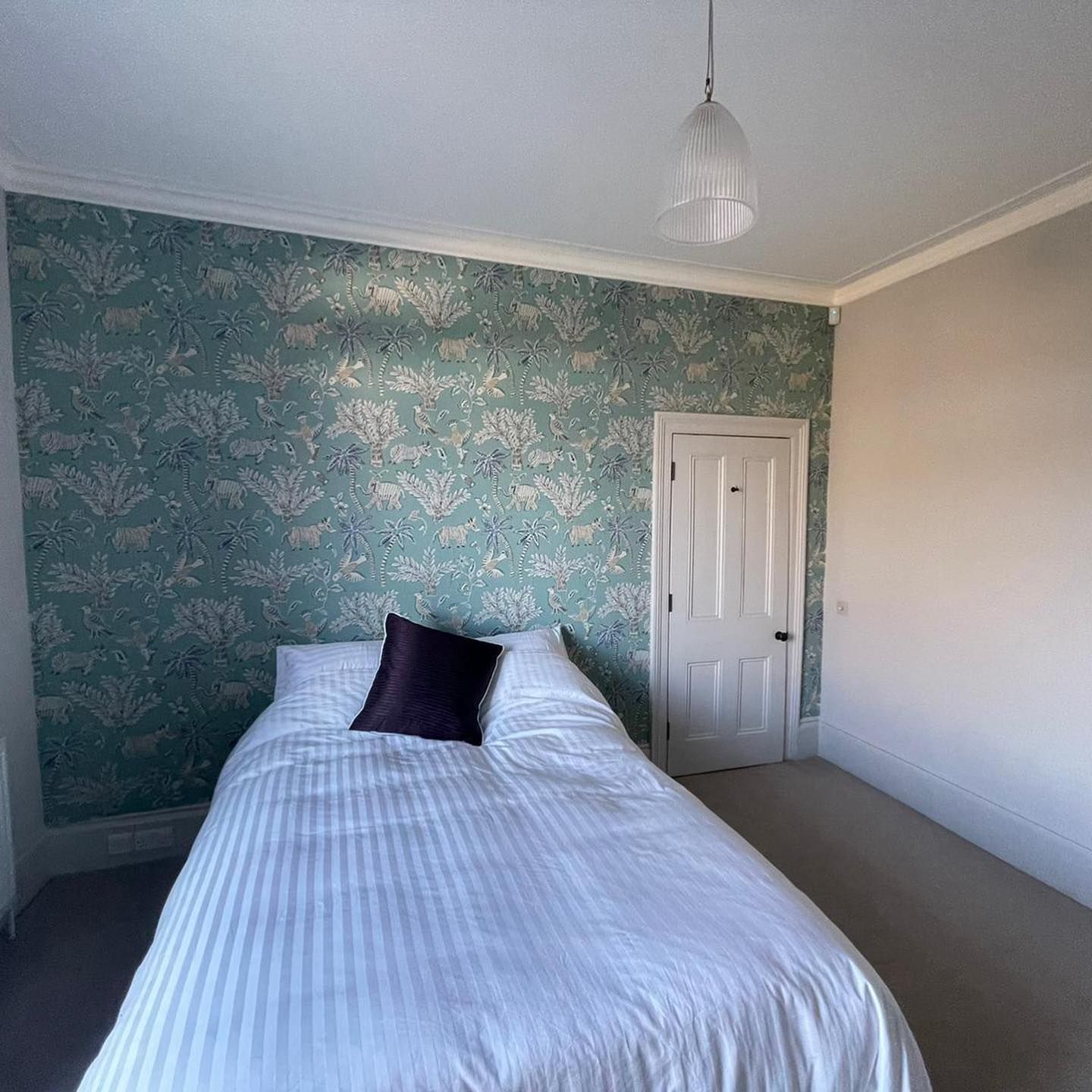 Bedroom with patterned teal wallpaper, bed, and white door.