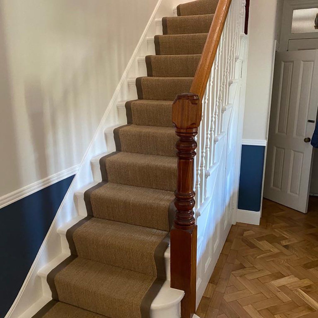A carpeted staircase with brown treads and white risers, wooden railing, and hardwood floor.