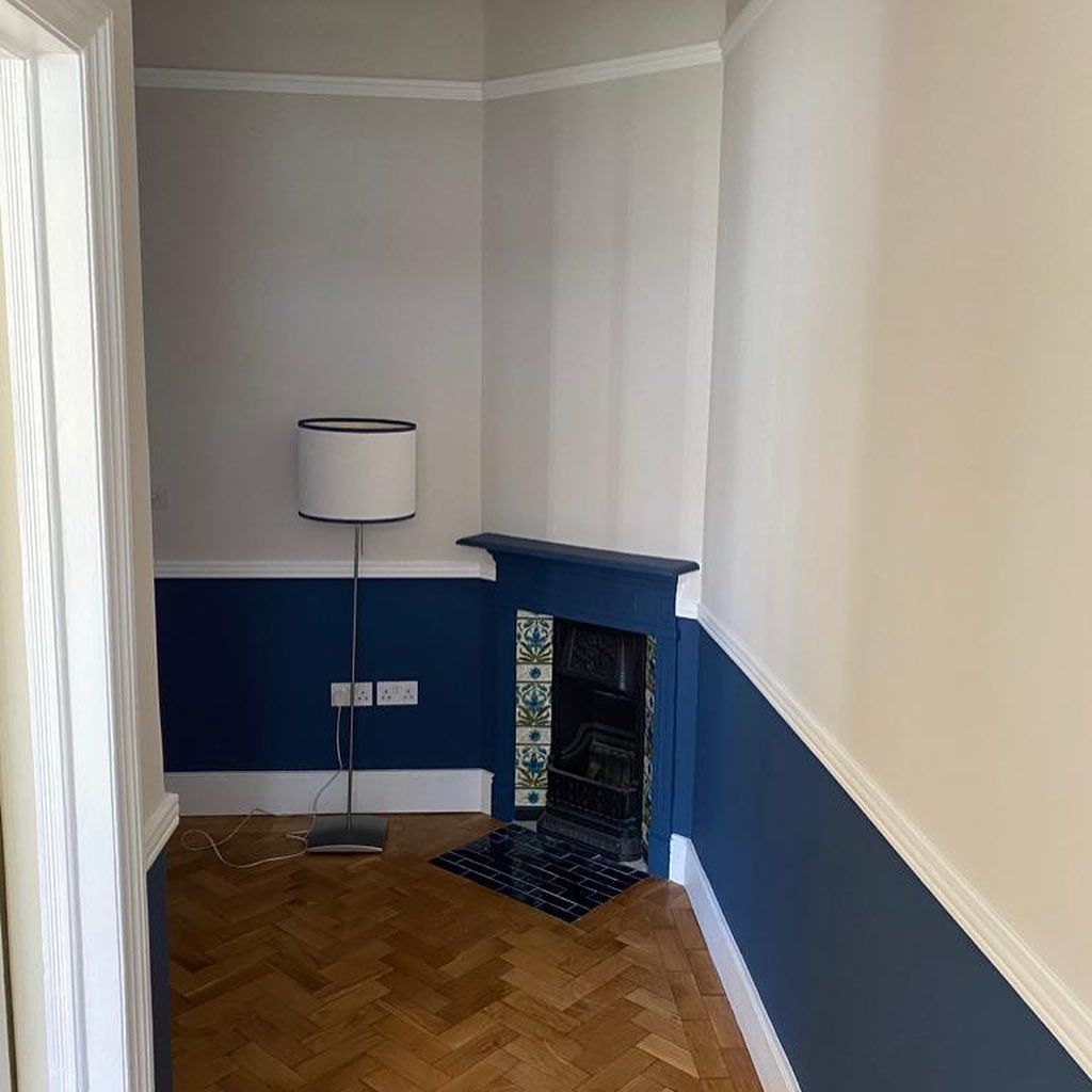 Room with blue and white walls, parquet flooring, and a fireplace. A lamp stands nearby.