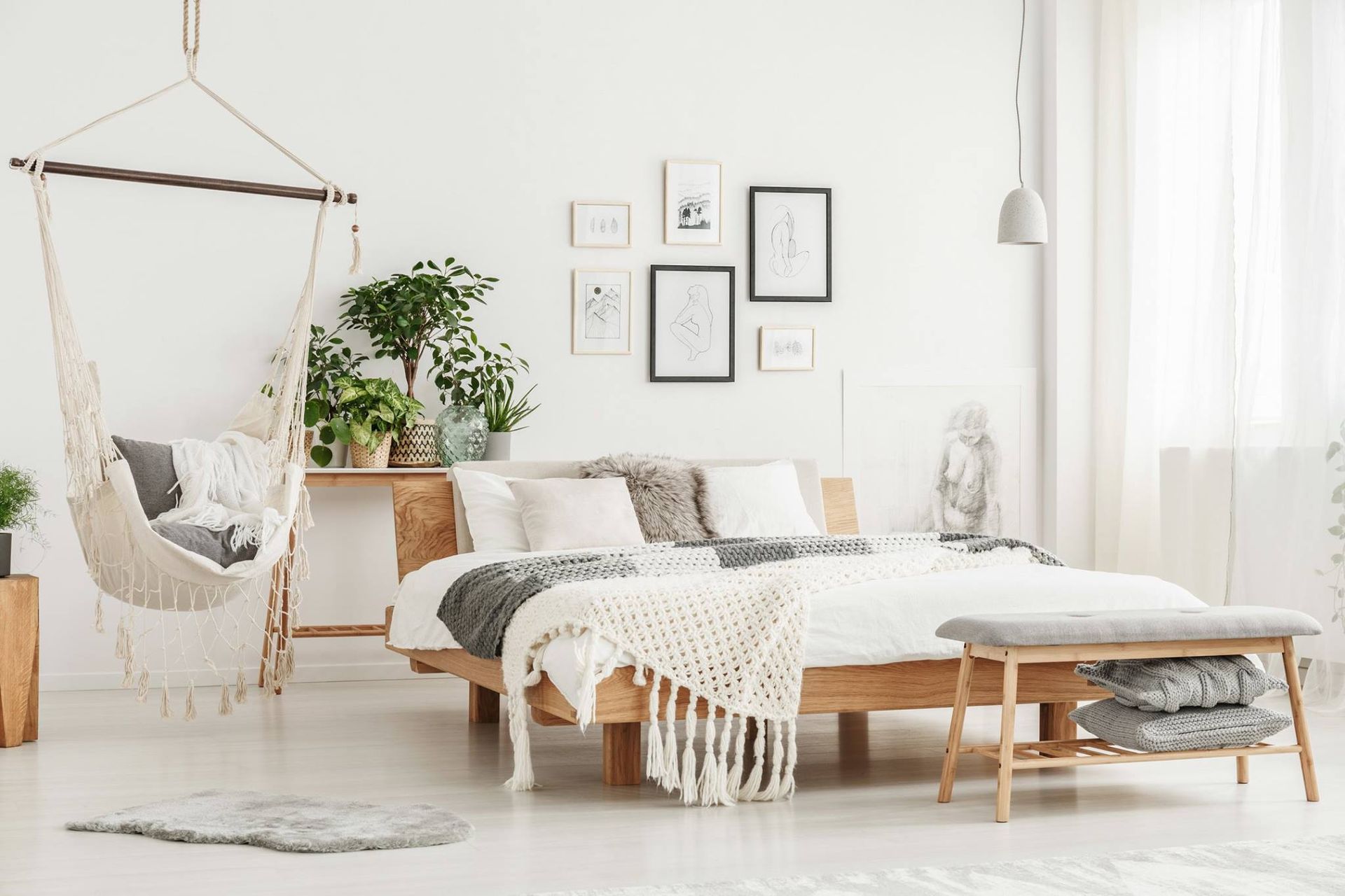 Bright bedroom with hanging chair, wooden bed, plants, and framed artwork.