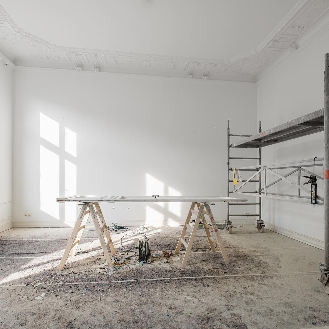 Room under renovation: white walls, scaffolding, sawhorses, bright sunlight, debris on floor.