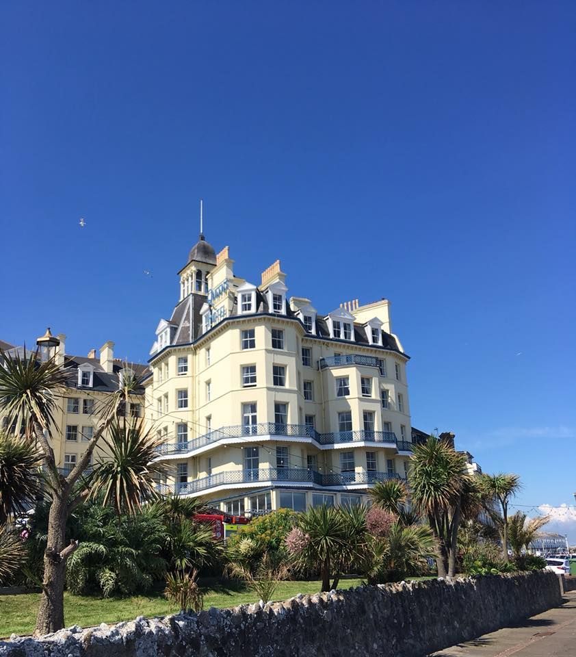 Large yellow building with balconies, blue sky, palm trees, and stone wall.