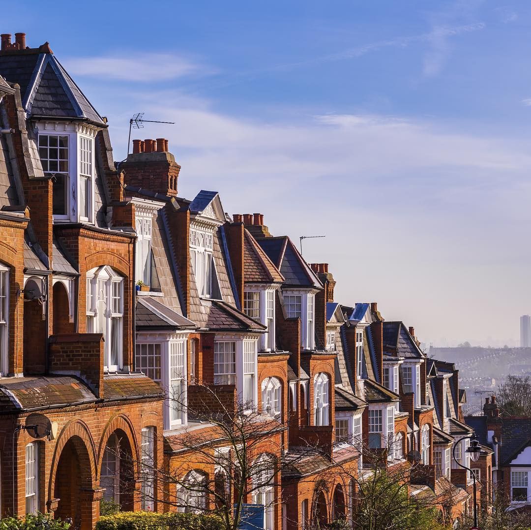 Row of red brick houses with bay windows under a blue sky.