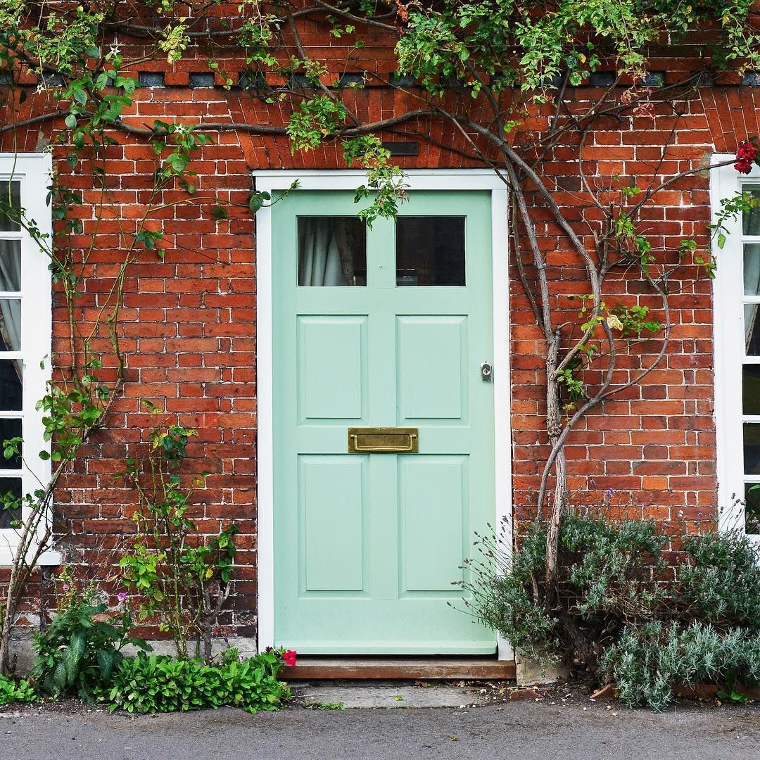 Brick house with a mint green door, windows on each side, and climbing plants.