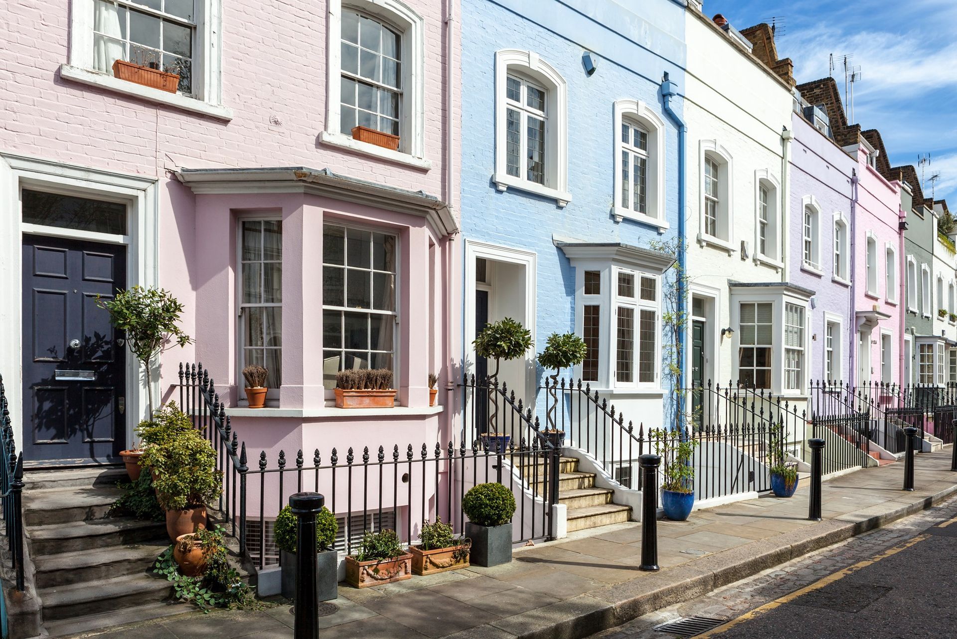 Row of colorful houses with pink, blue, and white facades and black railings in an urban setting.