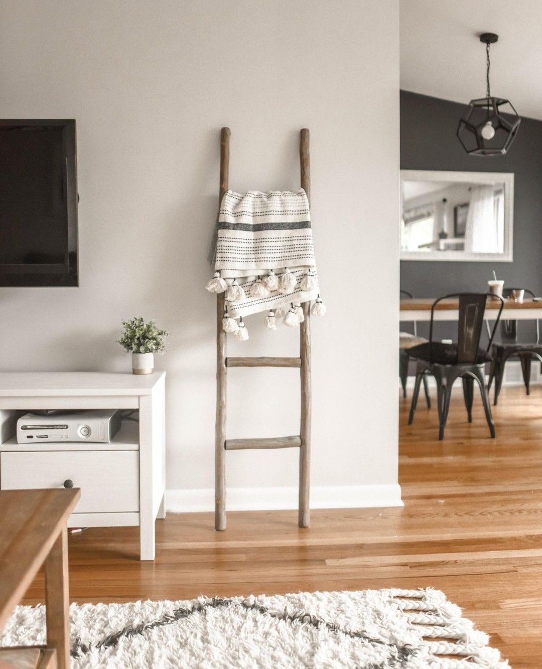 Wooden ladder with a blanket leans against a gray wall in a living room, near a TV and a white cabinet.
