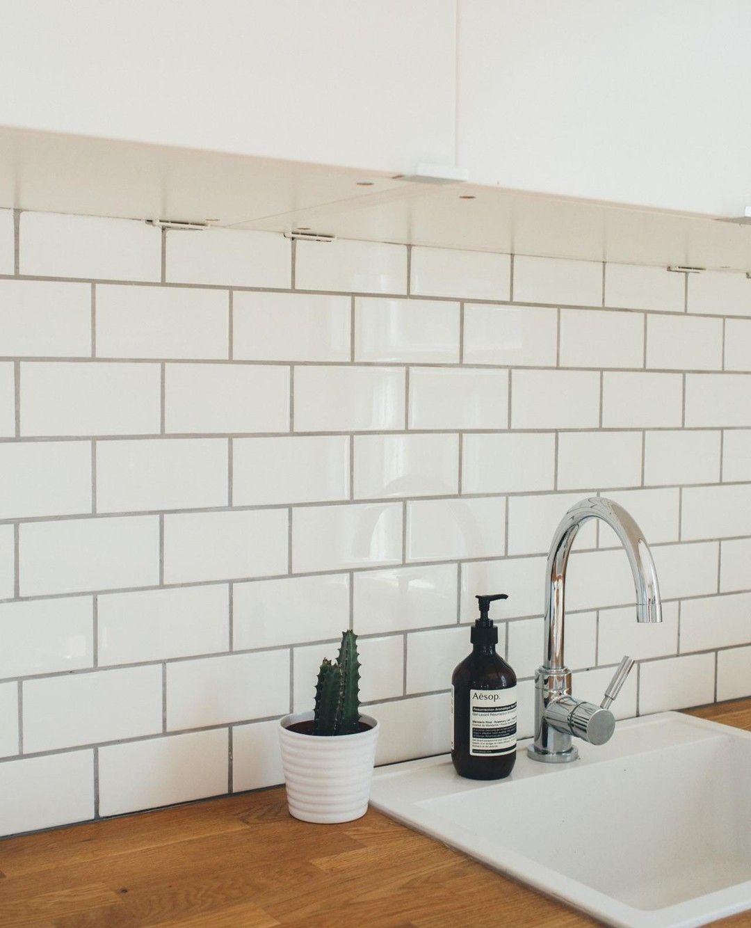 White tiled backsplash with sink, faucet, soap dispenser, and potted cactus on a wooden countertop.