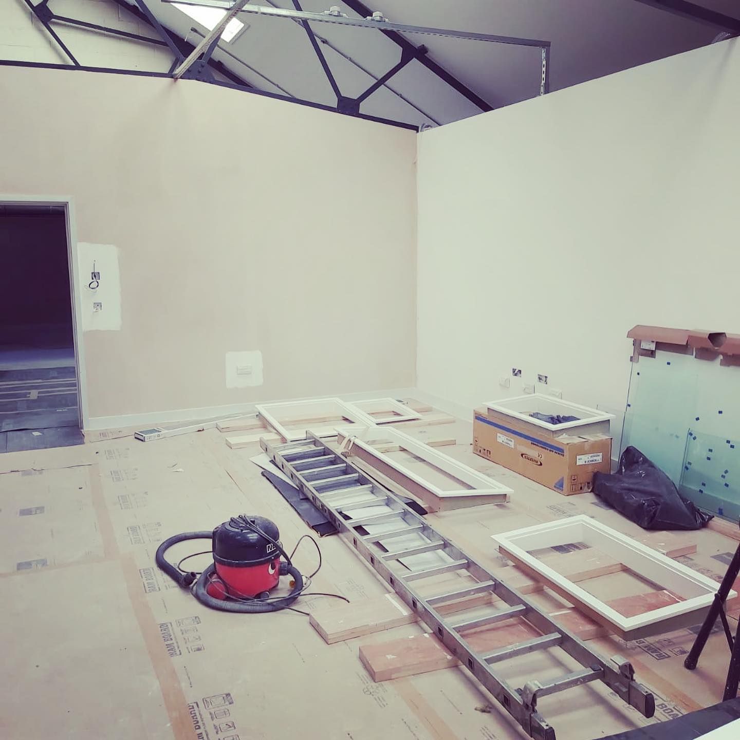 Interior construction: Room with bare walls, ladder, vacuum, windows, and debris on the floor.