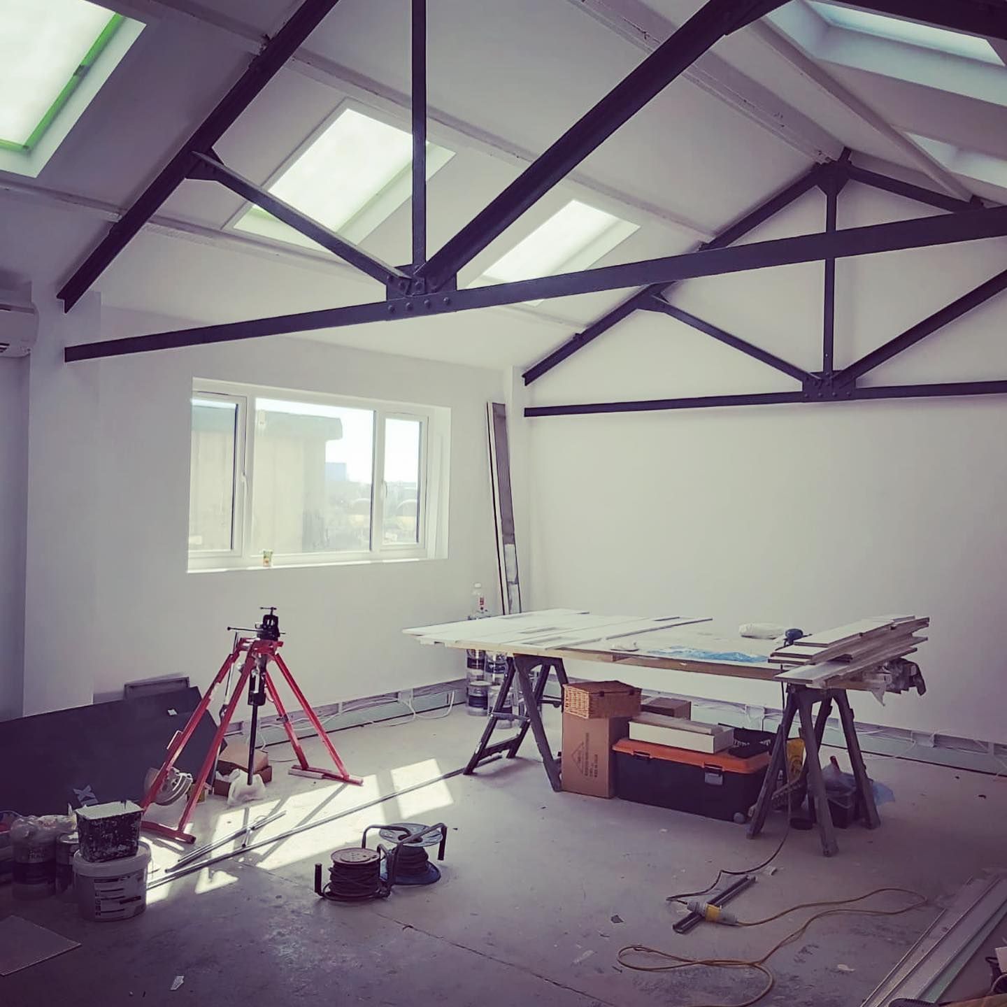 Interior of a renovated room. White walls, skylights, exposed metal beams, work table with tools.