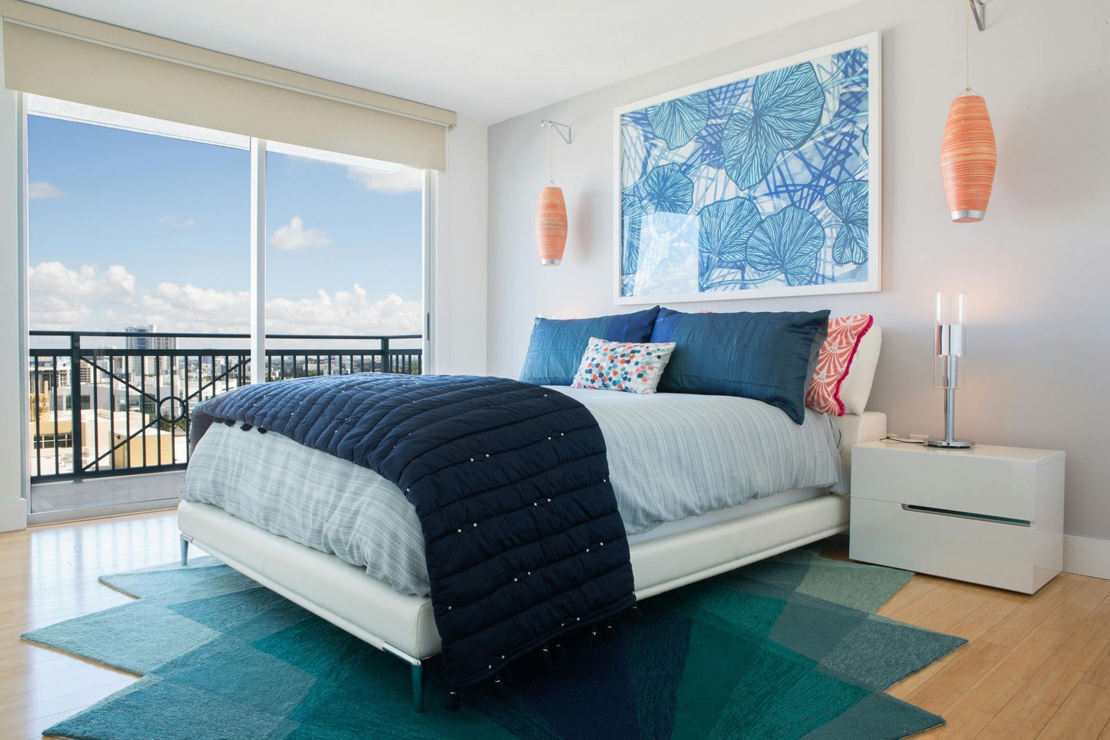 Bedroom with blue and white decor, large window, bed with blue blanket and pillows, teal rug.