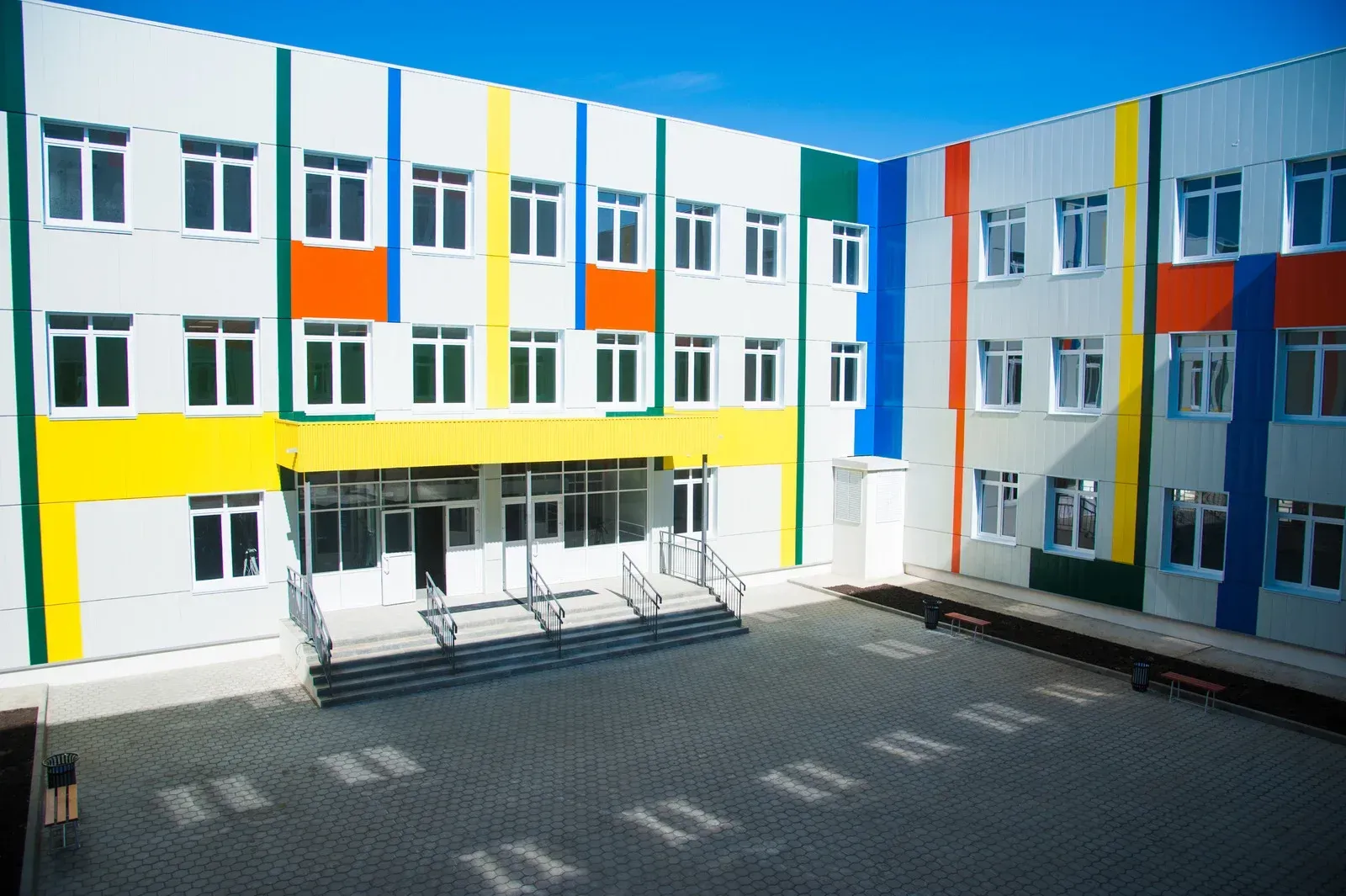 Exterior of a colorful school building. White with vertical stripes of orange, yellow, green, and blue.