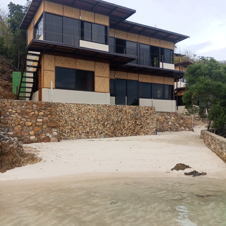 A large house sits on top of a hill next to a beach