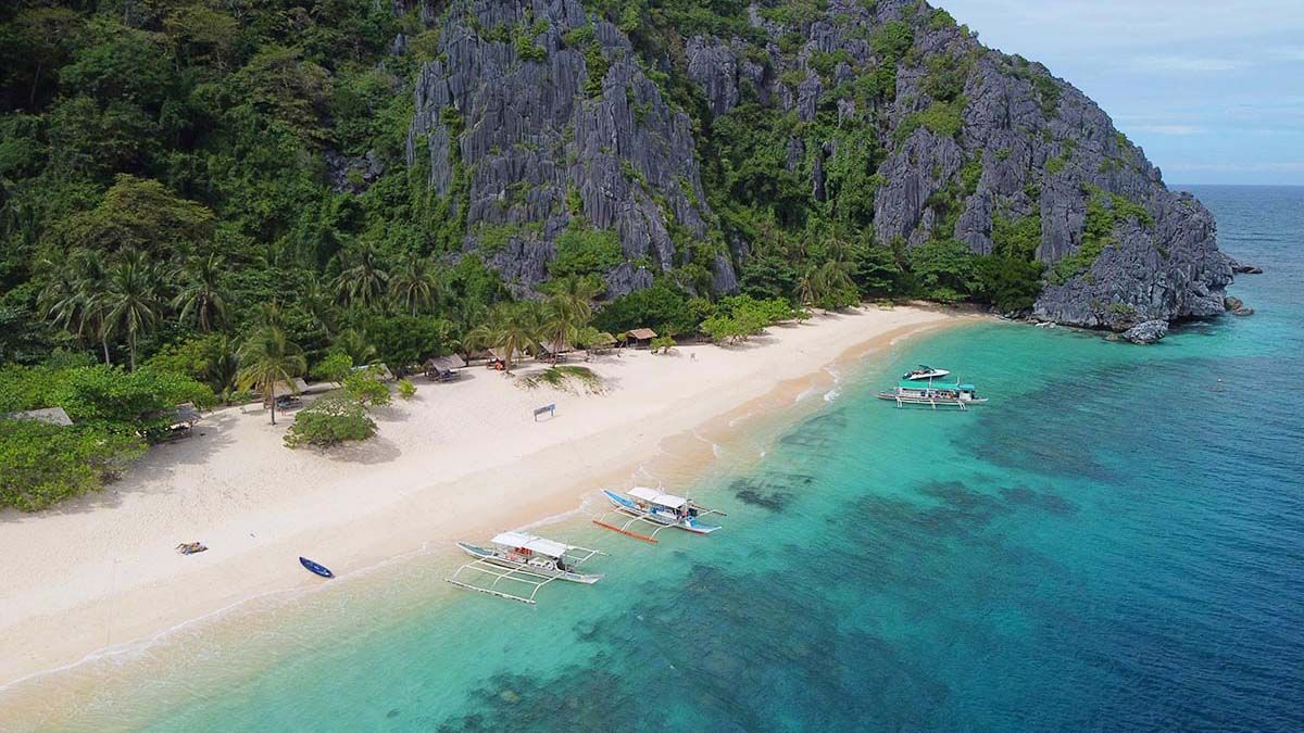 A beach with a boat in the water and a cliff in the background.