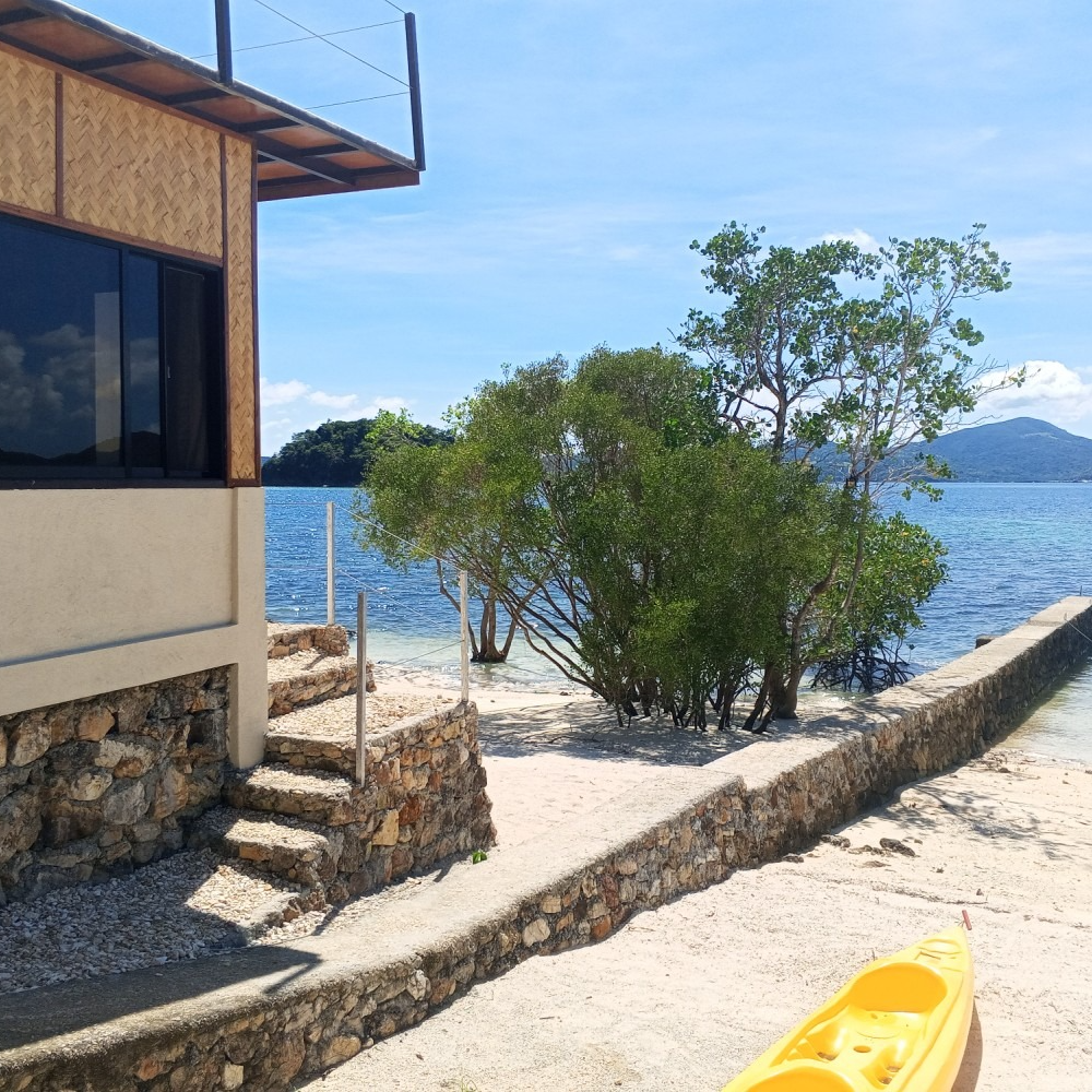 A yellow kayak sits on the beach near a house