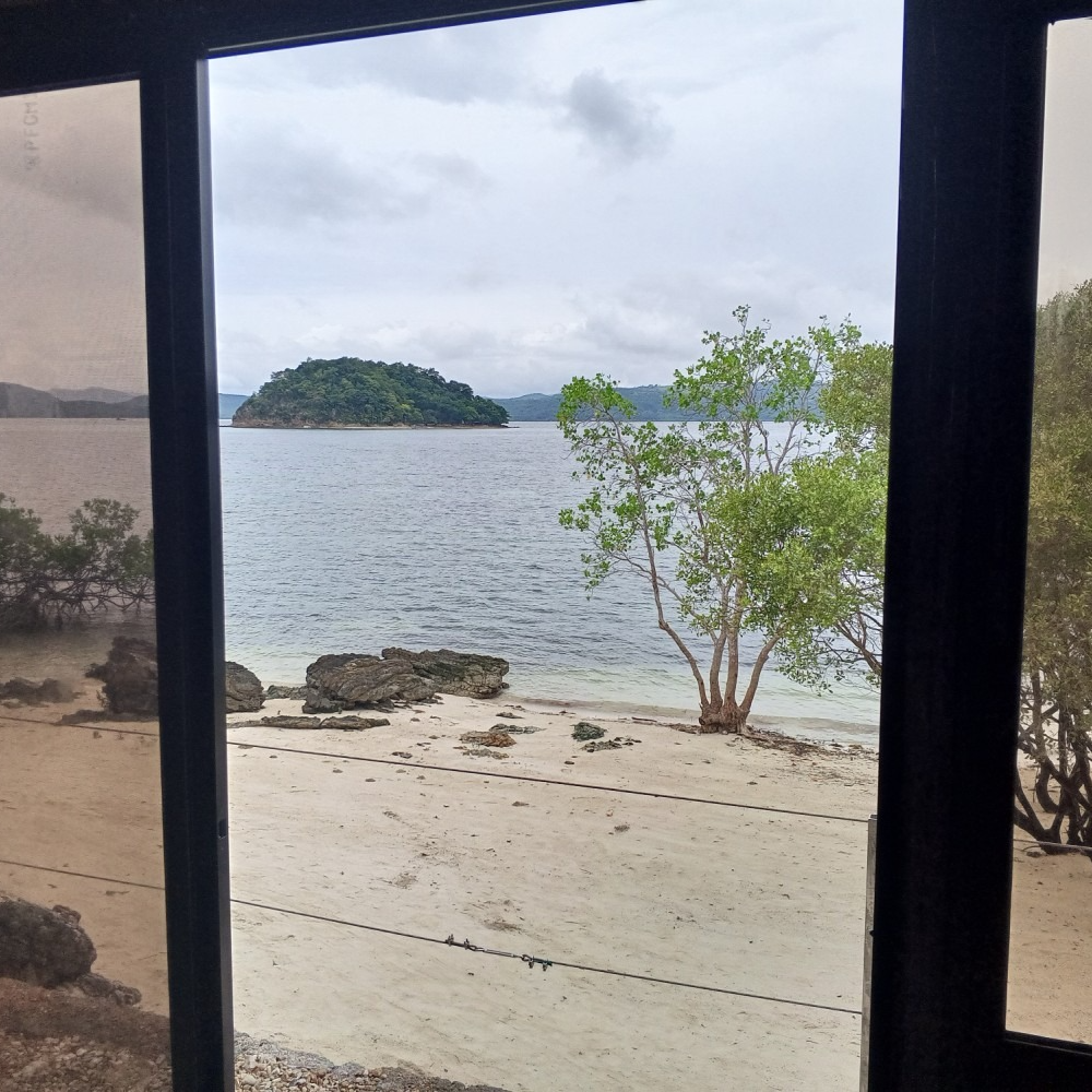 A view of a beach from a window with a small island in the distance