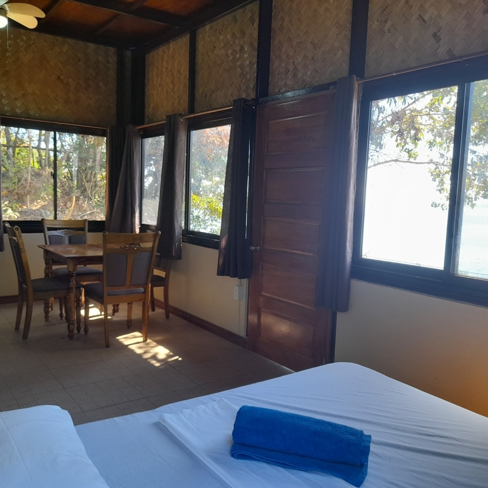 A bedroom with a table and chairs and a blue towel on the bed