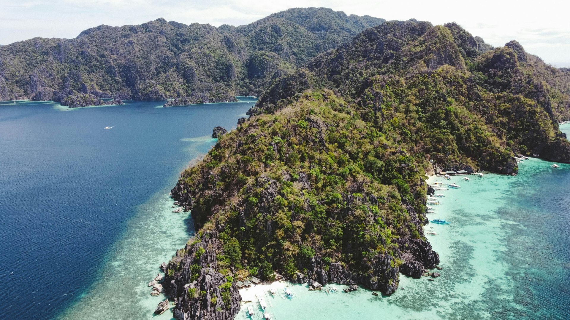 An aerial view of a small island in the middle of the ocean surrounded by mountains.