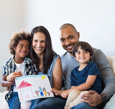 A family is sitting on a couch holding a drawing of their family.